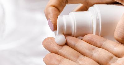 One hand squishing a lotion from the tube onto the other